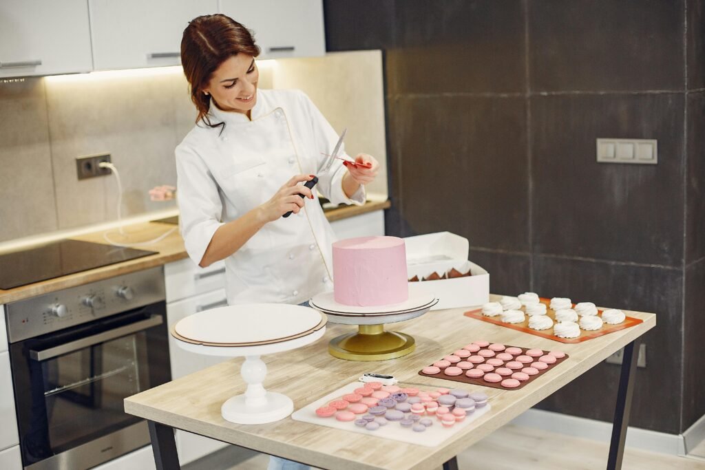 Female chef decorates cake with scissors and tools in a modern kitchen.