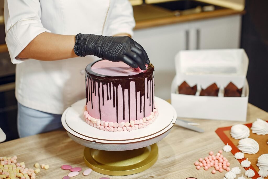 Unrecognizable female in apron and latex gloves garnishing delicious cake with sweet details while standing near table in modern restaurant
